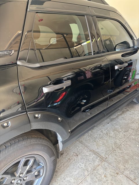 Black sedan with open door revealing interior, parked on concrete showing side profile and wheel