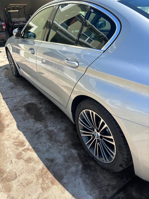 White sedan with open driver door and window, parked in lot showing side profile with alloy wheels