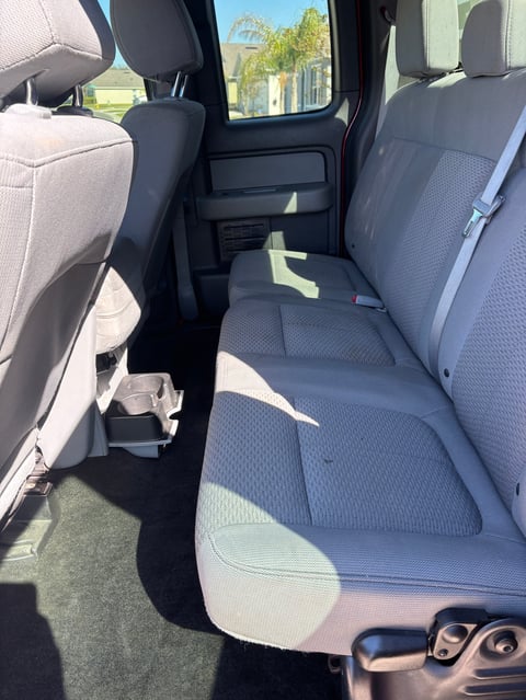 Interior of pickup truck showing rear bench seat with blue and gray upholstery and sunlight streaming through windows