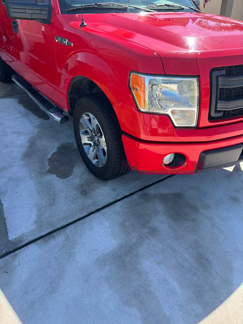 Red Ford F-150 pickup truck parked on concrete surface, front quarter view showing headlight and grille