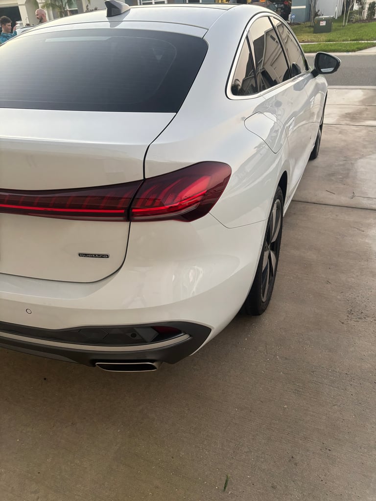 White sedan parked on driveway, rear view showing red taillights and chrome bumper