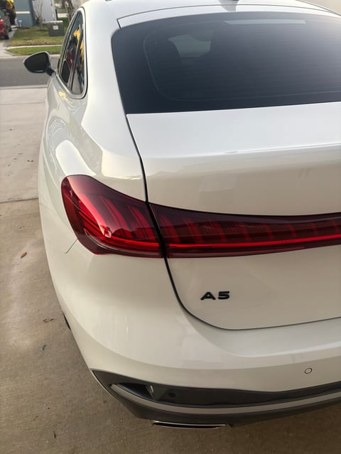 Rear view of white Audi A5 sedan showing tail lights and badge on a residential street