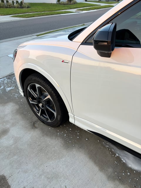 White sports car parked on wet driveway with alloy wheels and black mirror visible