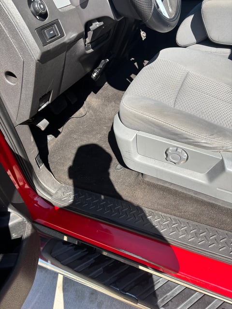 Interior view of a red car with open drivers door showing beige seats, steering wheel, and black floor mat
