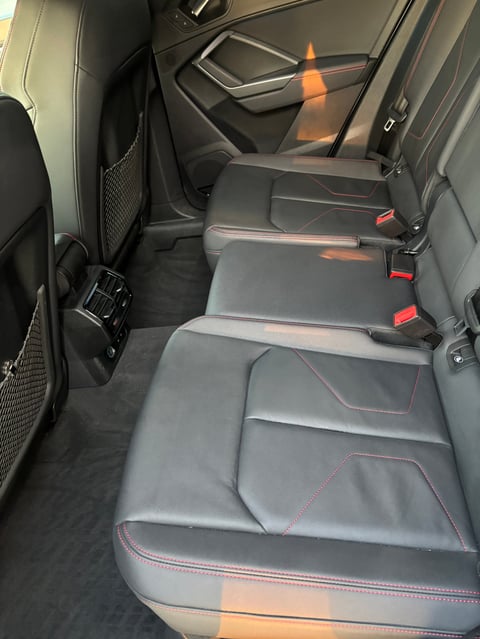 Car interior showing rear bench seats with gray upholstery, red stitching, and red seat belt buckles
