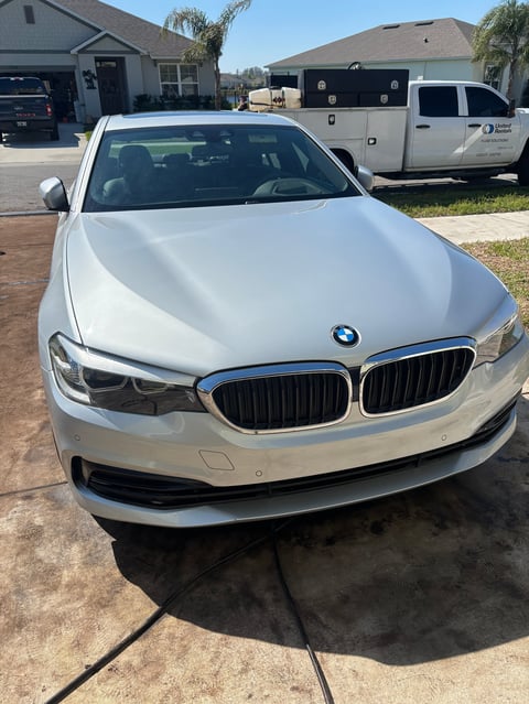 White BMW sedan parked on a driveway in front of residential homes and other vehicles