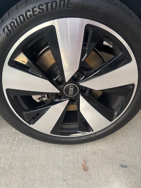 Black and white Audi alloy wheel with Bridgestone tire, featuring turbine-style spokes and center cap logo