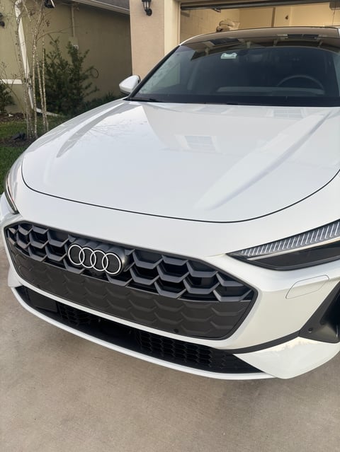 White Audi sedan parked in driveway, front view showing distinctive grille and LED headlights