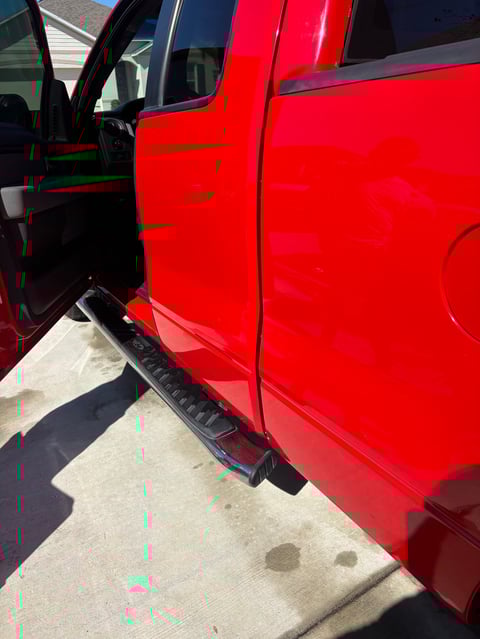 Red pickup truck with open driver side door and running board, parked on concrete surface in daylight