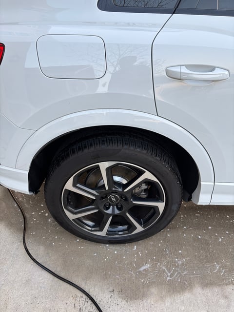 Close-up of white SUV wheel with black and silver alloy rim and tire on concrete ground