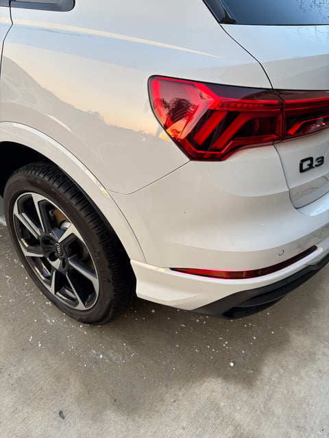 Close-up of white Audi Q3 car showing rear taillight, wheel, and bumper on pavement