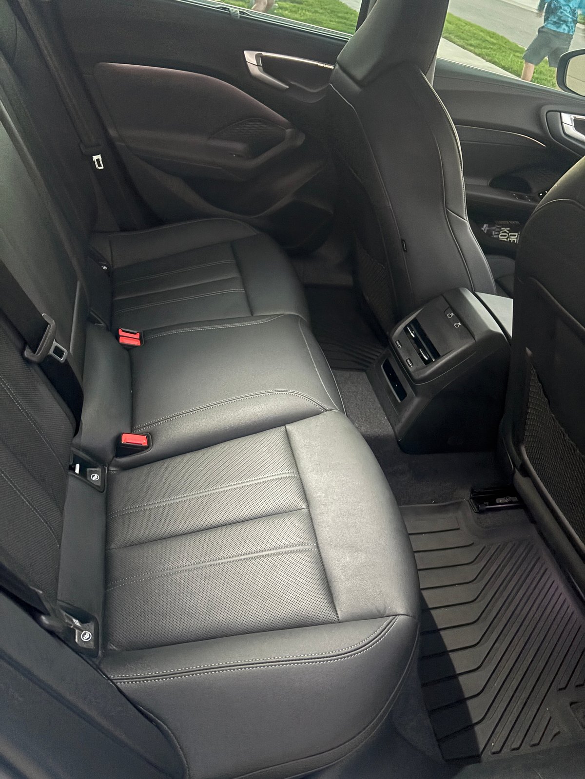 Interior view of a cars rear passenger seat with black leather upholstery and red safety belt anchors visible