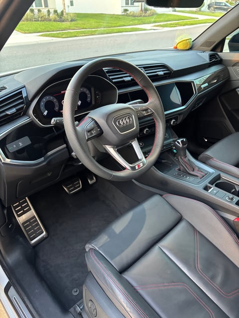 Interior of an Audi vehicle showing steering wheel, dashboard, touchscreen display, and leather seats viewed from drivers side