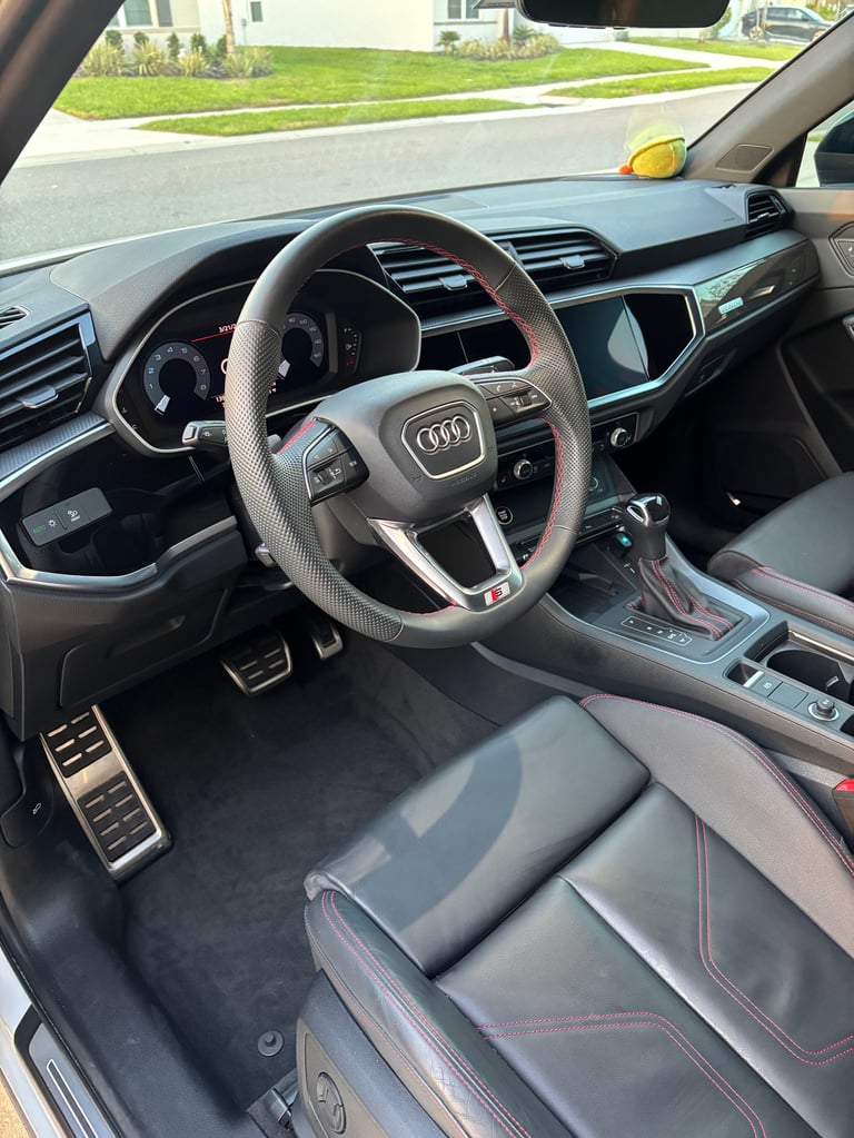 Interior of an Audi vehicle showing steering wheel, dashboard, touchscreen display, and leather seats viewed from drivers side