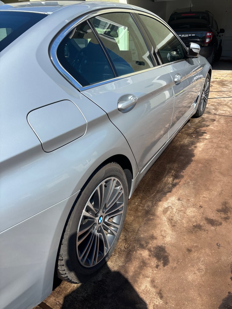 Silver BMW sedan parked on dirt ground, side view showing door, window, and alloy wheel with shadows visible